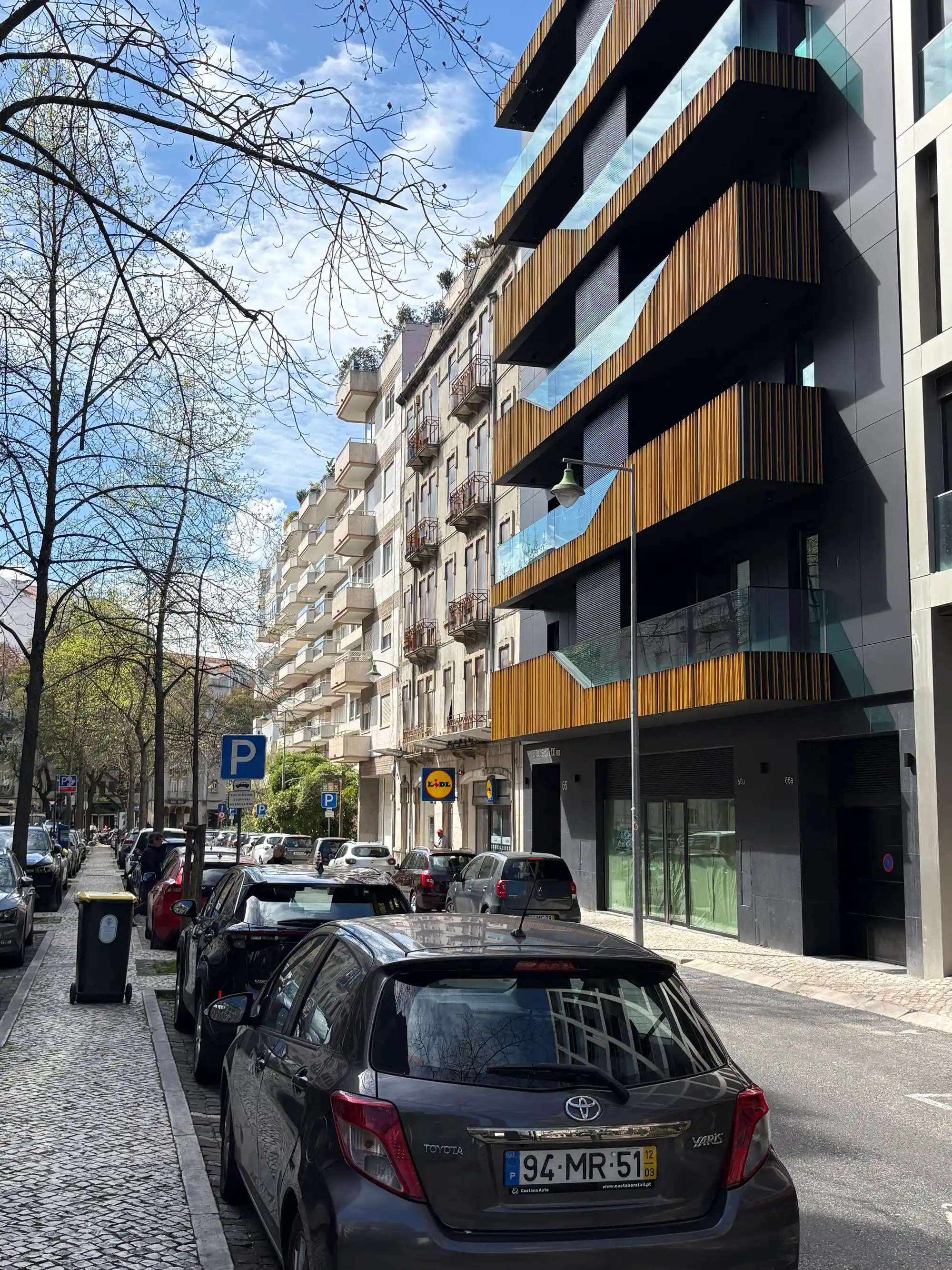 Prédio de apartamentos moderno com varandas e carros estacionados em uma rua na Avenida Novas, Lisboa, Portugal.