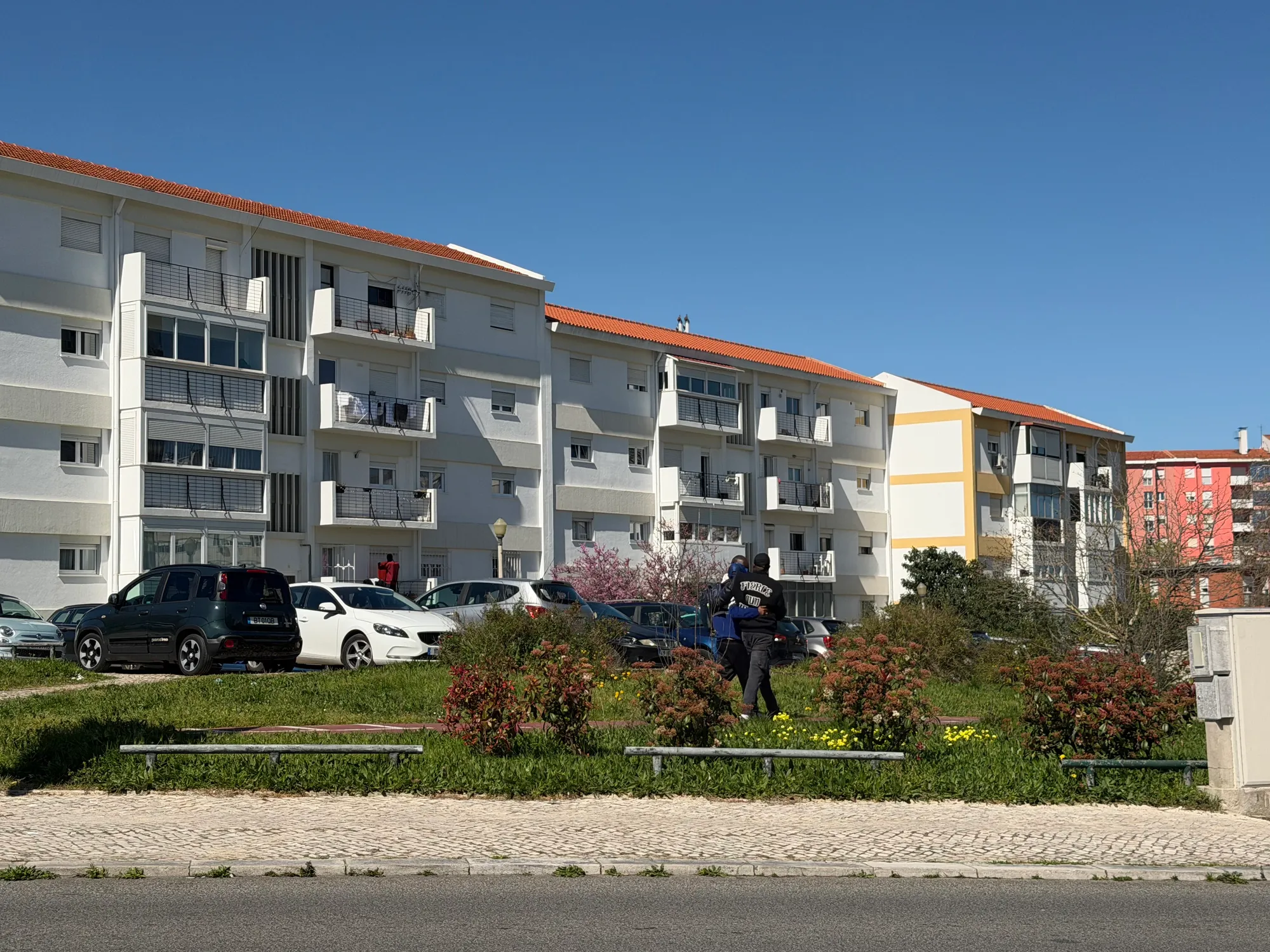 Olivais Lisbon residential buildings with parked cars, green area, and pedestrian walking along the street