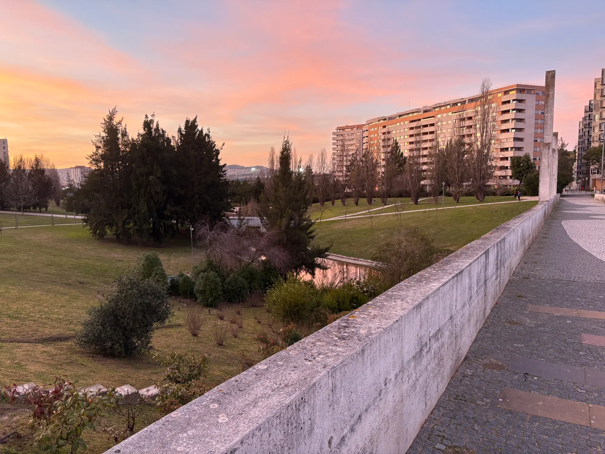 Santa Clara Lisbon park at sunset with green landscape, trees, and residential buildings under colorful sky